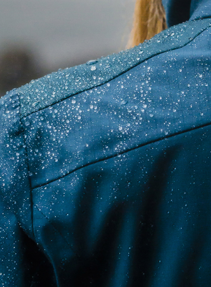 Water droplets beading on the shoulder of a blue technical wool jacket, with blonde hair behind