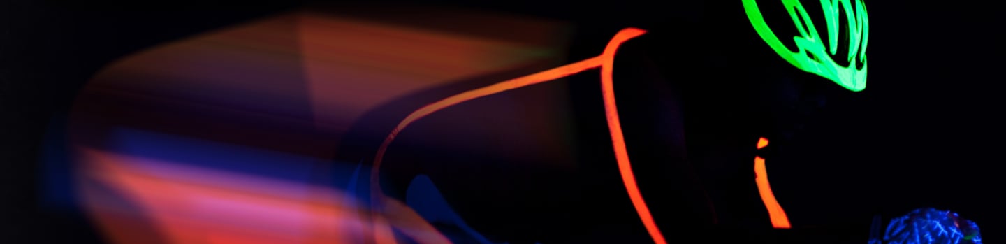 Cyclist in fluorescent outlines and green helmet glowing in the dark, with blurred motion trails